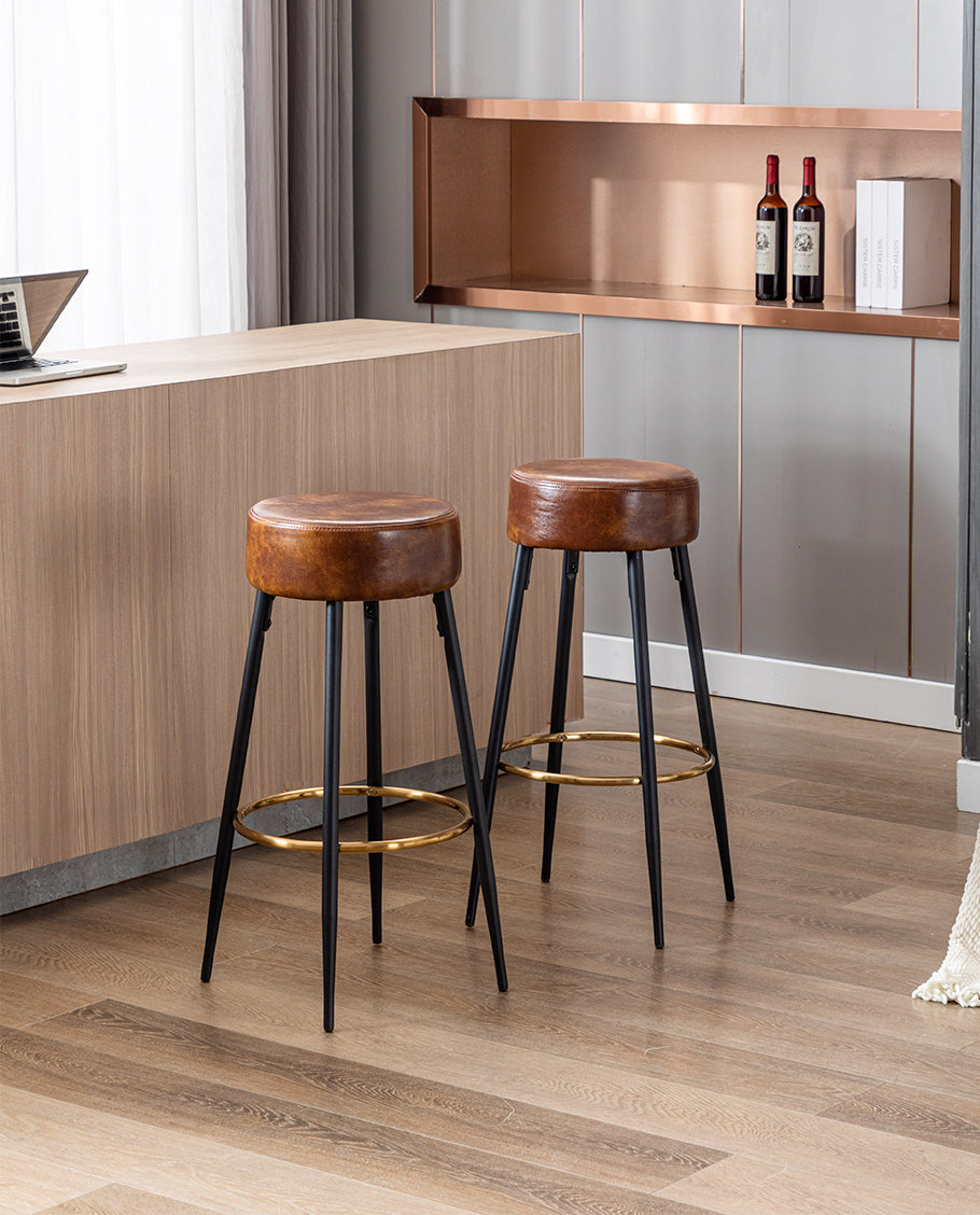 Pair of brown leather bar stools with black legs and gold footrests beside a wooden island.